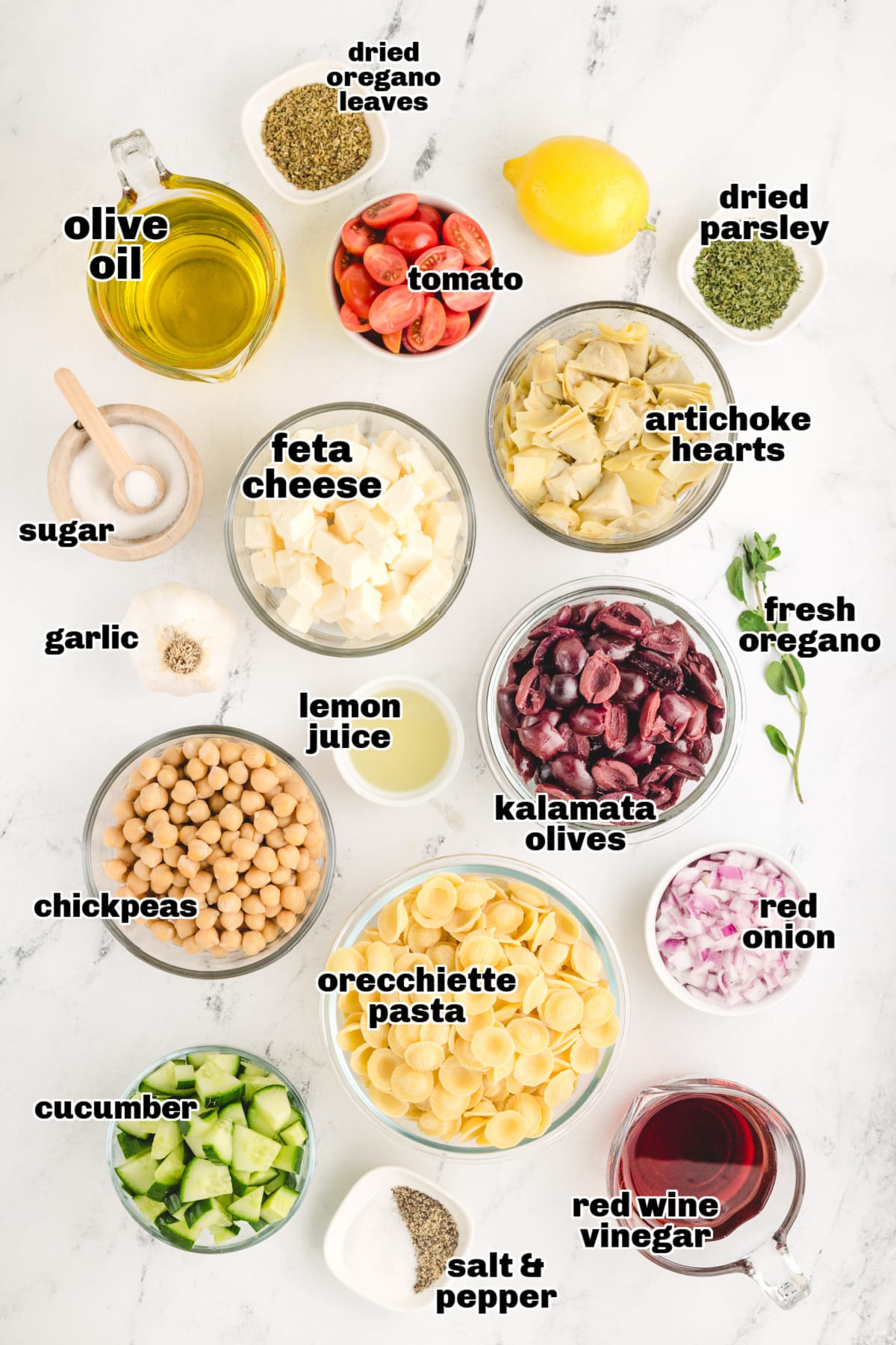 Greek Pasta Salad ingredients All the ingredients laid out on a countertop, including pasta, feta, olives, cucumbers, and dressing components.
