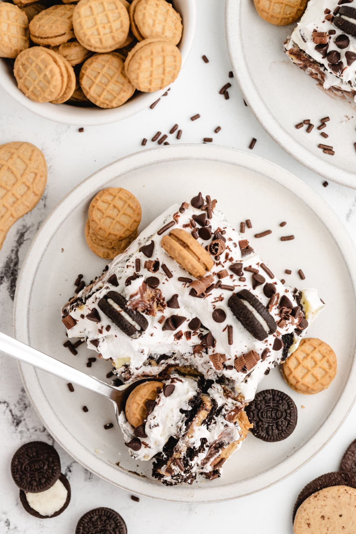 Plated slice of peanut butter chocolate icebox cake with cookie topping Single slice of layered no-bake peanut butter Oreo dessert with whipped topping and sprinkles