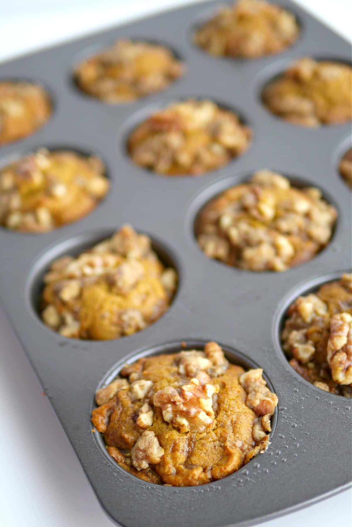 Pumpkin brown sugar muffins fresh out of the oven in a muffin tin with walnut crumble tops.
