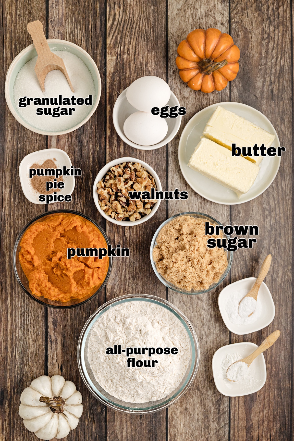 Ingredients for brown sugar pumpkin muffins arranged on a wooden table, including pumpkin purée, butter, flour, and walnuts.