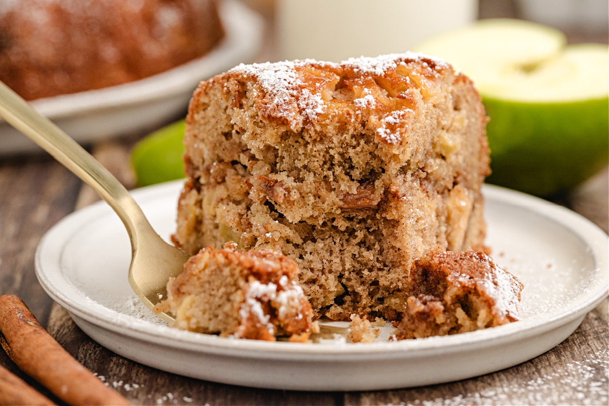 Apple bundt cake slice on a plate with powdered sugar and a glass bottle of milk
