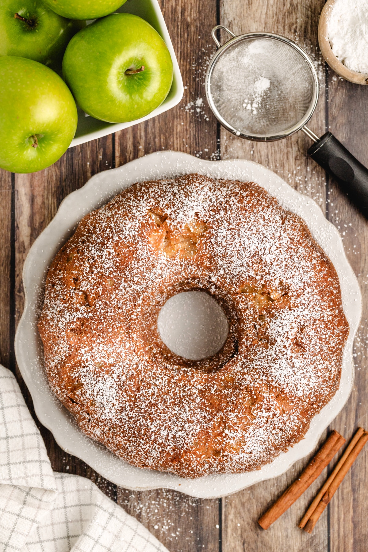 Brown sugar cinnamon apple bundt cake dusted with confectioners’ sugar next to fresh apples