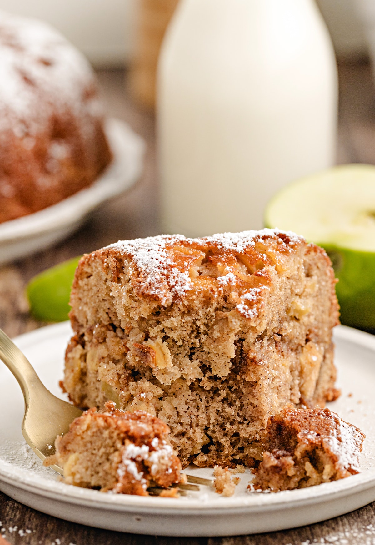 Slice of brown sugar cinnamon apple bundt cake with Granny Smith apples and cinnamon sticks on a plate