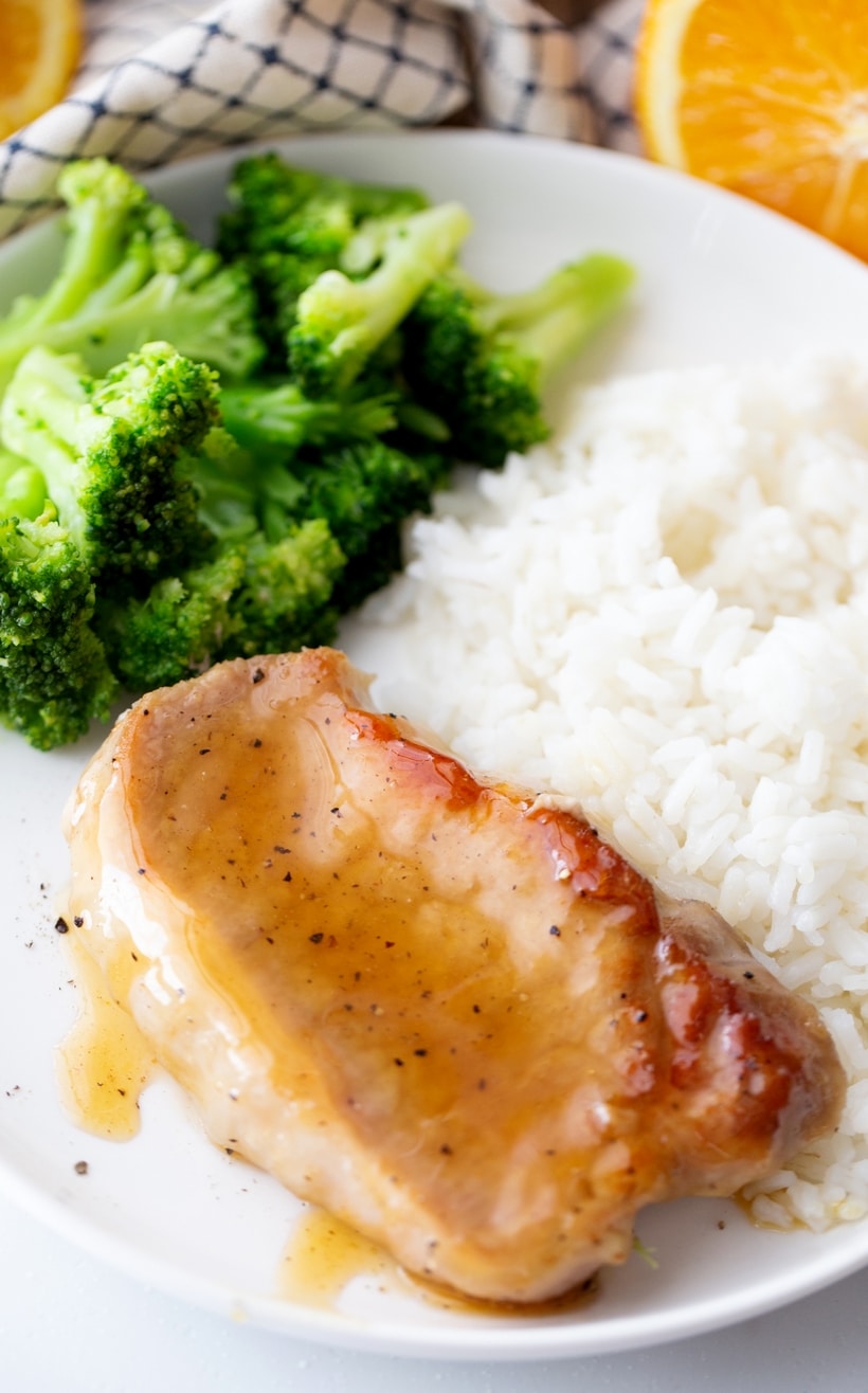 Orange Glazed Pork Chops with only five ingredients are ready in minutes and make a delicious dinner on a weeknight or weekend. Glaed pork chop sitting on a plate with rice and broccoli.