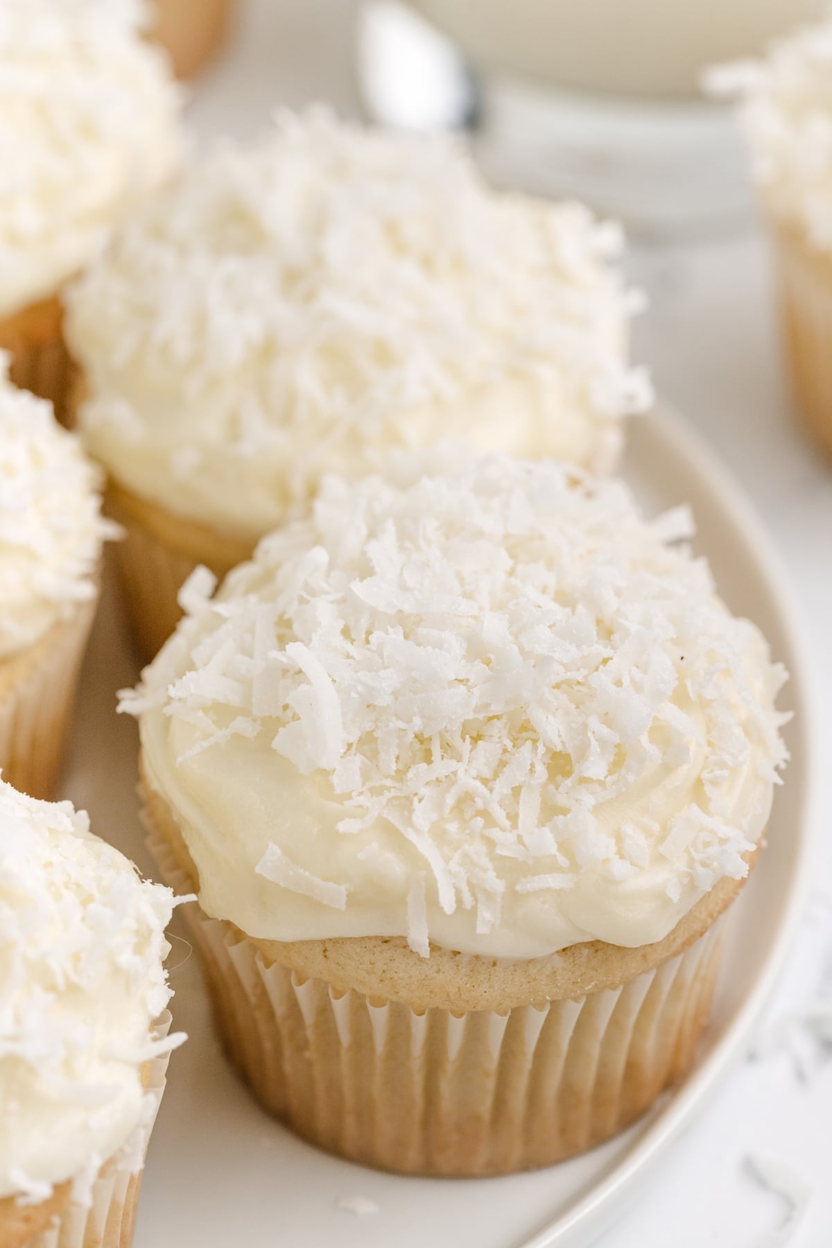 Coconut Cupcakes with Coconut Cream Cheese Frosting on a plate Coconut cupcakes with a soft, moist texture and a coconut cream cheese frosting swirl, garnished with coconut flakes.