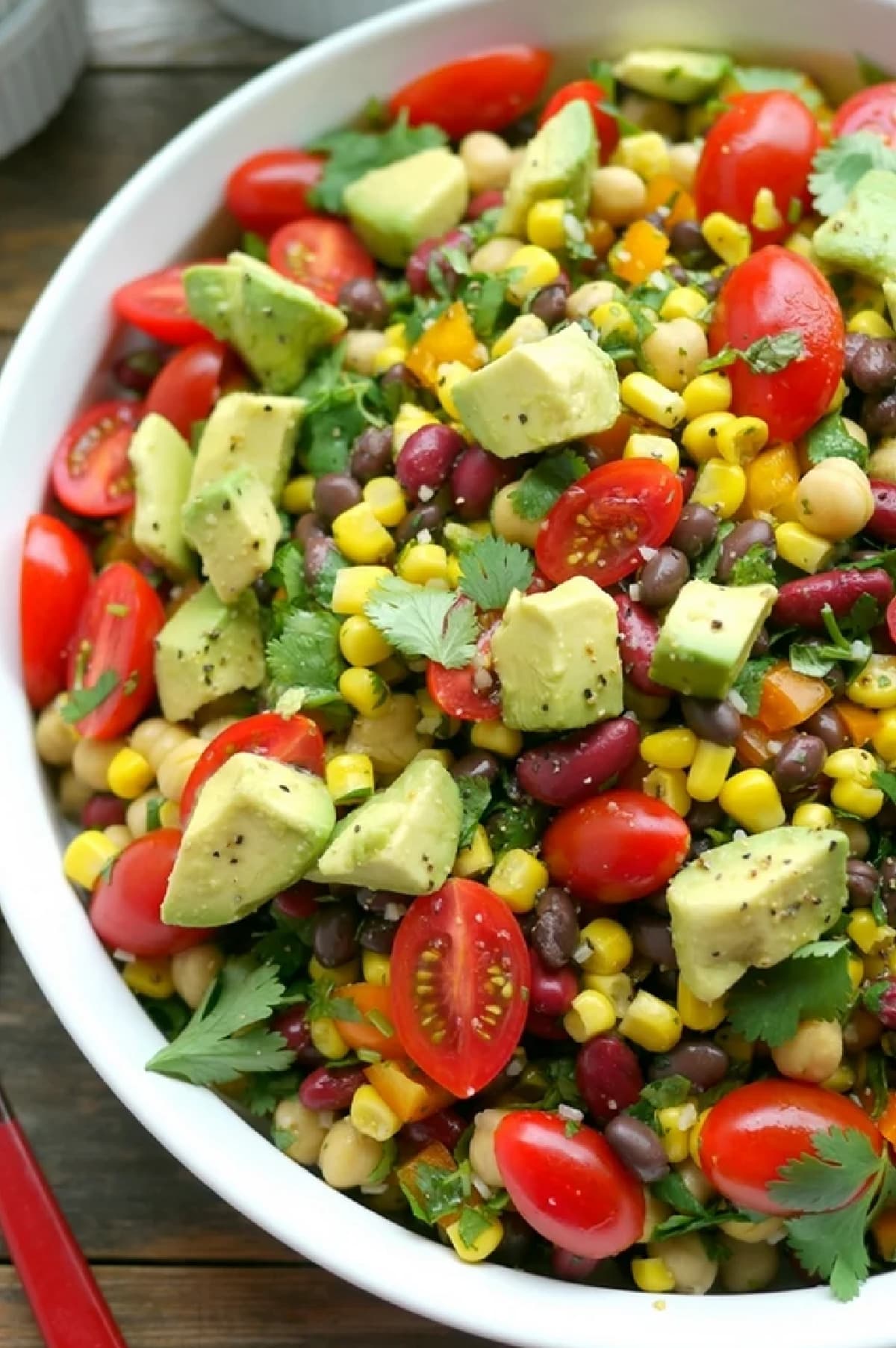 Top view of the avocado and three bean salad in a bowl, showing a mix of black beans, kidney beans, garbanzo beans, corn, diced bell pepper, tomatoes, and avocado.