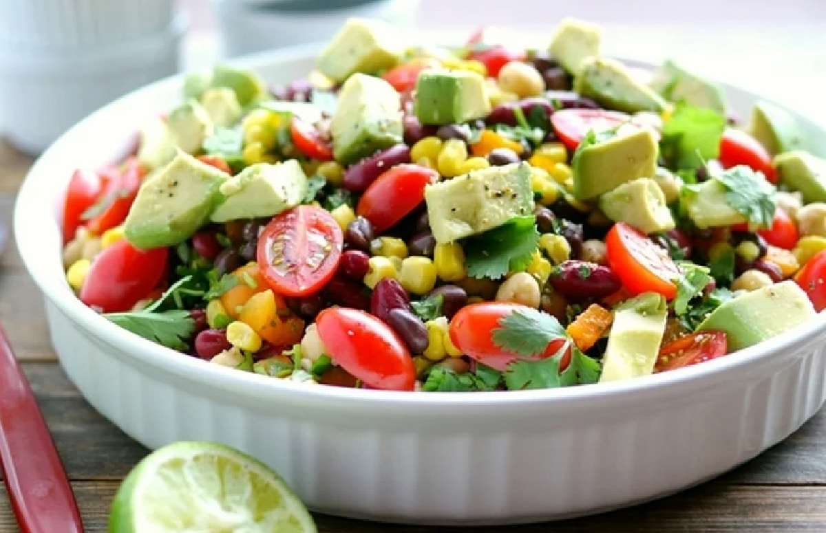 Close-up top view of the salad, highlighting creamy avocado chunks and bright red grape tomatoes mixed with beans and fresh cilantro.