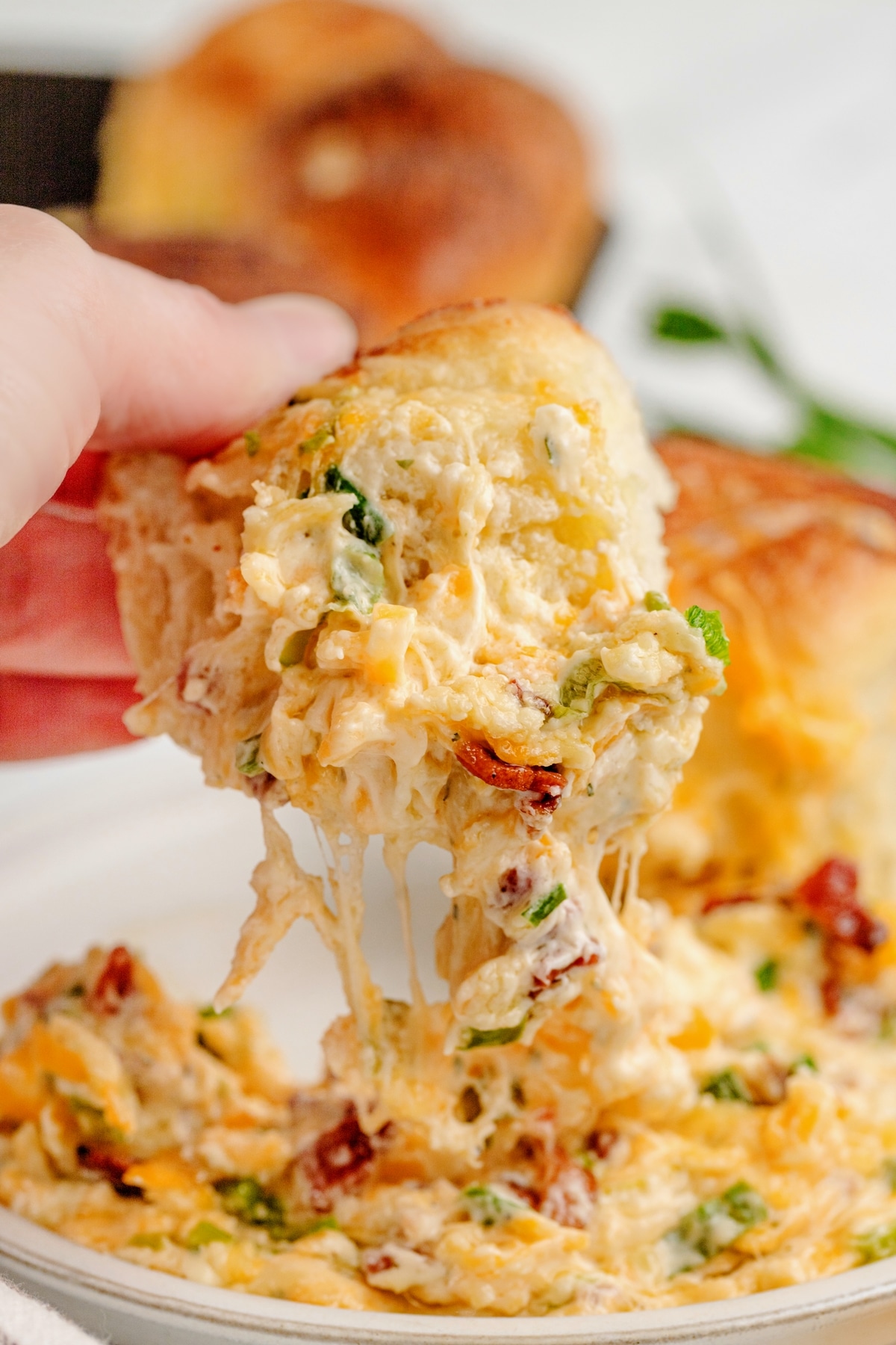 Serving Sour Cream Bacon Ranch Dip with Dinner Rolls Hand scooping a serving of sour cream bacon ranch dip from the center of a ring of golden-brown dinner rolls.