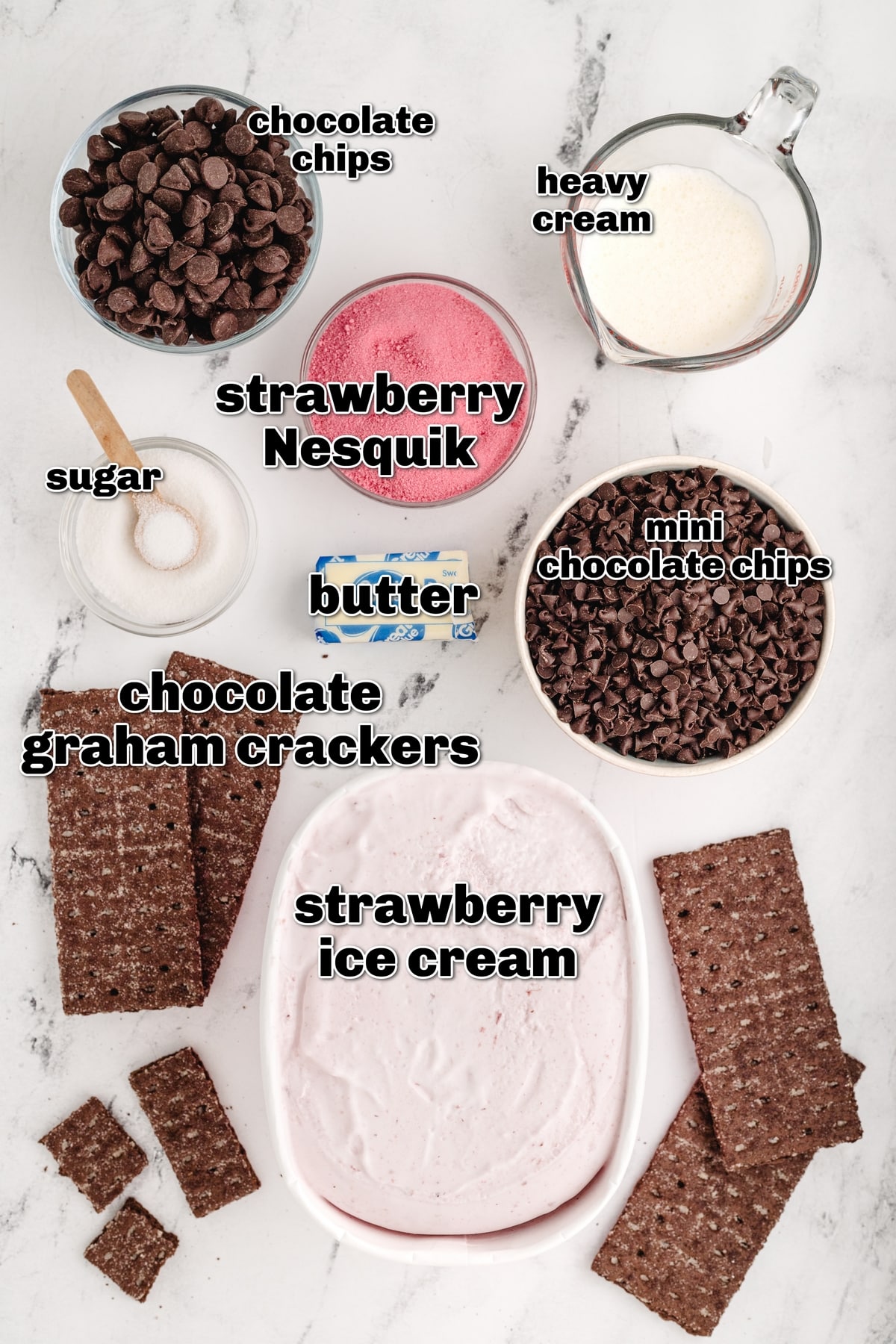 Strawberry Chocolate Chip Ice Cream Cake ingredients A flat lay of all the ingredients including chocolate graham crackers, strawberry ice cream, mini chocolate chips, strawberry milk powder, heavy cream, and semi-sweet chocolate chips.
