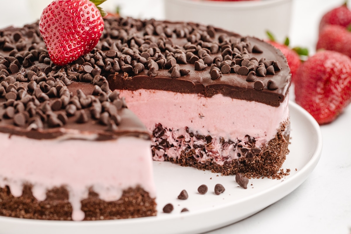 Strawberry Chocolate Chip Ice Cream Cake sliced A strawberry chocolate chip ice cream cake with a slice removed, revealing the layers of crust, ice cream, and ganache, with extra chocolate chips sprinkled on top for Noble Pig