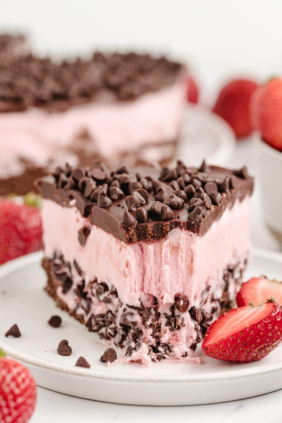 Strawberry Chocolate Chip Ice Cream Cake slice A partially eaten slice of strawberry chocolate chip ice cream cake on a plate, showing layers of chocolate graham cracker crust, creamy strawberry ice cream with mini chocolate chips, and a glossy chocolate ganache topping for Noble Pig