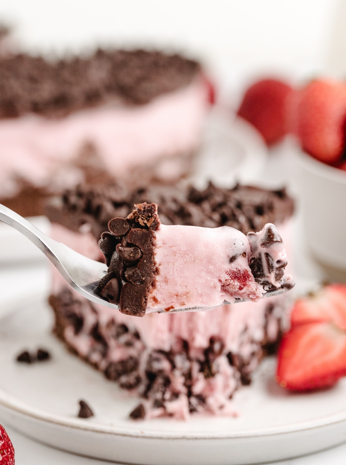 Strawberry Chocolate Chip Ice Cream Cake a bite A fork lifting a bite of strawberry chocolate chip ice cream cake, showing the creamy ice cream and chocolate ganache with flecks of mini chocolate chips.