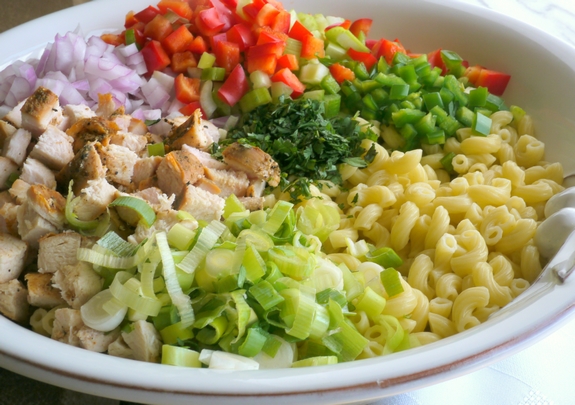 This Kicked-Up Chicken-Macaroni Salad recipe will impress your family and friends at your next picnic, BBQ or tailgate. This chicken macaroni salad pairs well with almost anything and will have your guests begging for more. Macaroni salad ingredients together in a bowl before being mixed.