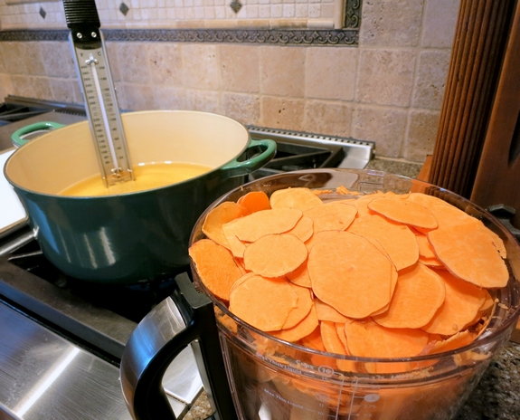 Sliced sweet potaoes in a bowl with a candy thermometer in a Dutch oven filled with oil.
