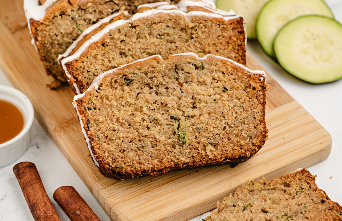 Sliced honey zucchini loaf with cinnamon sticks and zucchini in the background