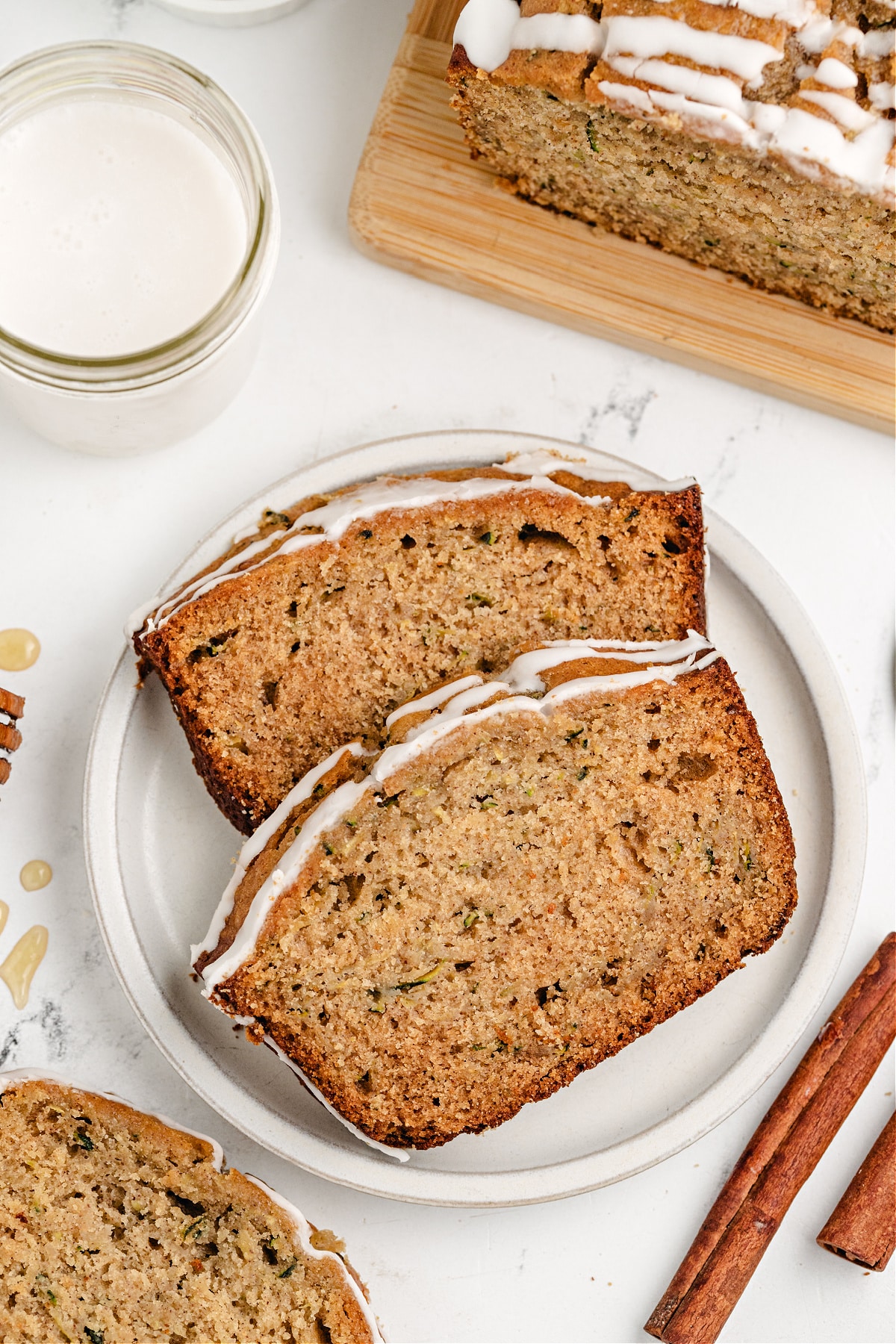  Two slices of honey zucchini bread on a plate with glaze and a glass of milk