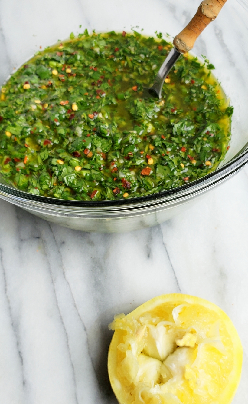 Chimichurri in a bowl with a spoon and a squeezed half of a lemon.