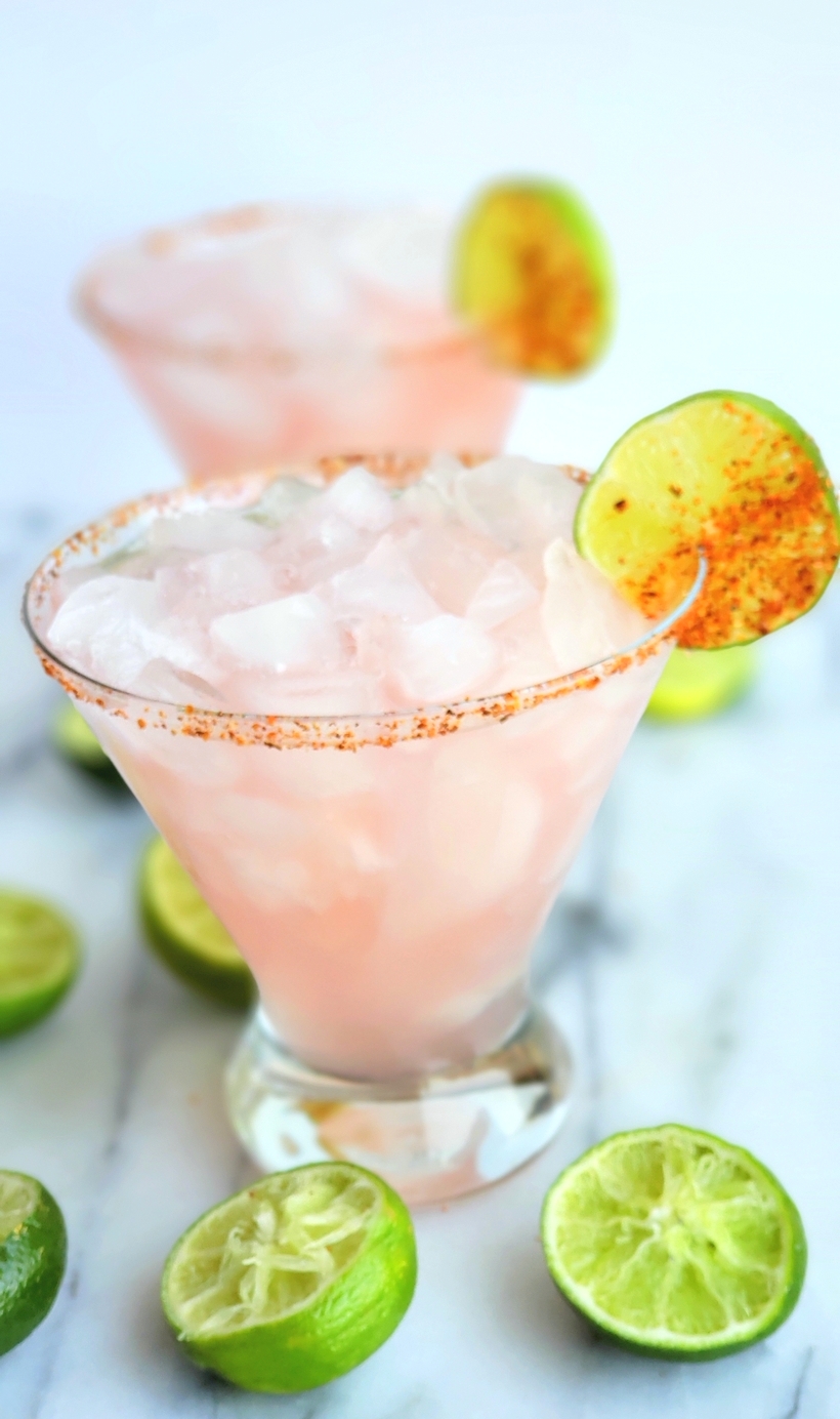 The petal pink color of this Icy Hibiscus Margarita is alluring, but it's the sweet, tangy and refreshing flavor that will have you asking for a second pour. #noblepig #margarita #cocktail #hibiscus Two Hibiscus margaritas with squeezed limes around them.