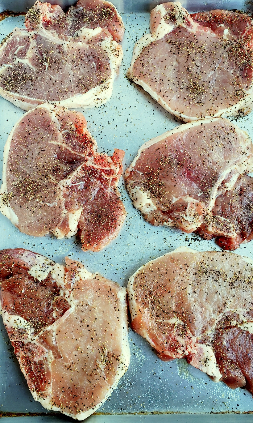Grilling a quick and easy meal has never been so easy. These tender and Juicy Grilled Pork Chops with Spicy Peach Glaze come together quickly for a dinner your family and friends will not soon forget. The glaze can be put together in minutes, while the pork chops undergo a quick brine. #noblepig #pork #porkchops #grilling #easydinners Six raw pork chops on a baking sheet seasoned with salt and pepper.