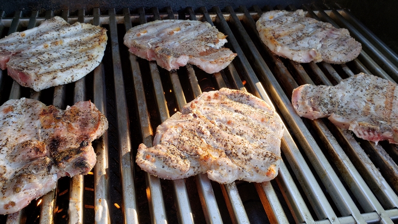 Grilling a quick and easy meal has never been so easy. These tender and Juicy Grilled Pork Chops with Spicy Peach Glaze come together quickly for a dinner your family and friends will not soon forget. The glaze can be put together in minutes, while the pork chops undergo a quick brine. #noblepig #pork #porkchops #grilling #easydinners Pork chops cooking on a grill.
