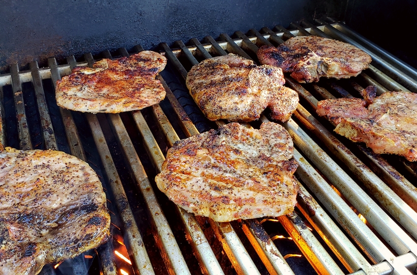 Grilling a quick and easy meal has never been so easy. These tender and Juicy Grilled Pork Chops with Spicy Peach Glaze come together quickly for a dinner your family and friends will not soon forget. The glaze can be put together in minutes, while the pork chops undergo a quick brine. #noblepig #pork #porkchops #grilling #easydinners Pork chops cooking on a grill.