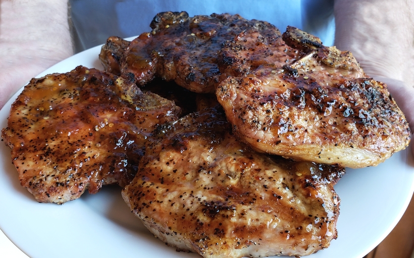 Grilling a quick and easy meal has never been so easy. These tender and Juicy Grilled Pork Chops with Spicy Peach Glaze come together quickly for a dinner your family and friends will not soon forget. The glaze can be put together in minutes, while the pork chops undergo a quick brine. #noblepig #pork #porkchops #grilling #easydinners Pork chops on a platter.