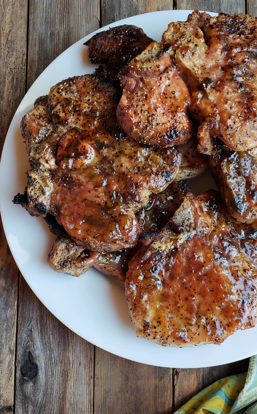 Grilling a quick and easy meal has never been so easy. These tender and Juicy Grilled Pork Chops with Spicy Peach Glaze come together quickly for a dinner your family and friends will not soon forget. The glaze can be put together in minutes, while the pork chops undergo a quick brine. #noblepig #pork #porkchops #grilling #easydinners Pork chops on a white plate.