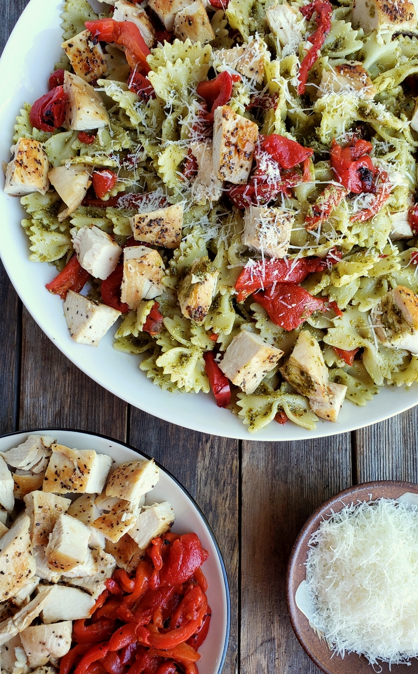 Get dinner on the table with this Quick Chicken and Pesto Pasta. It's full of flavor and makes great leftovers for lunch. Chicken pesto pasta in a white bowl surrounded by a bowl of chicken and red peppers and grated parmesan cheese.