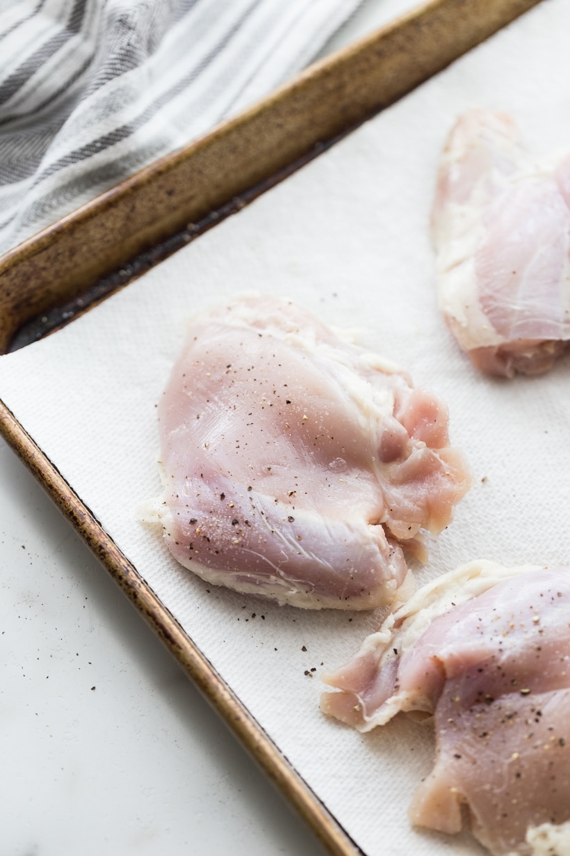 Raw chicken thighs laid out on a baking sheet, prepped for seasoning.