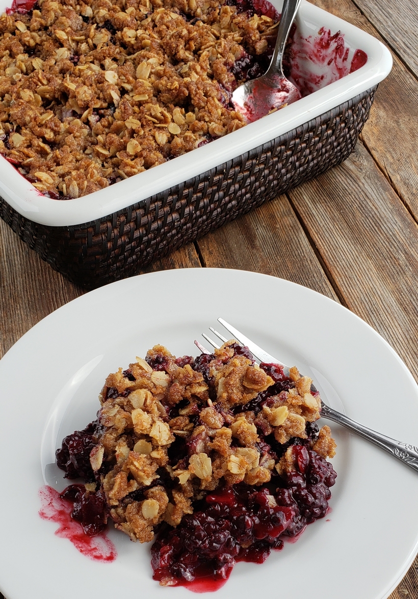 Nothing tastes more like late summer than a Blackberry Crumble. Even if you've never baked from scratch, you will find this recipe so easy to put together. #noblepig #blackberry #crumble #summerdessert A serving of blackberry crumble on a white plate with serving dish in the background.