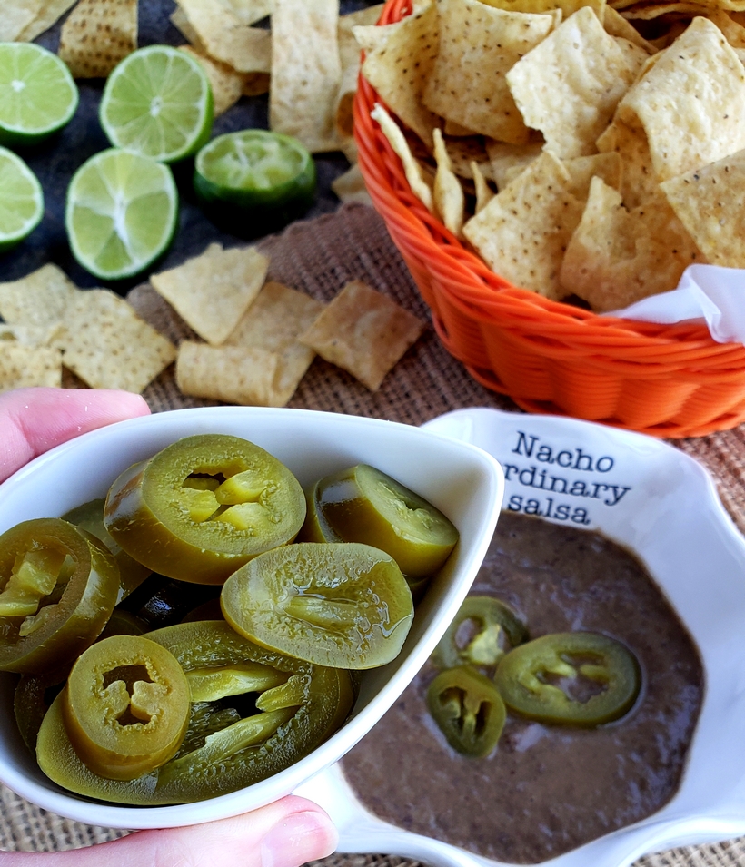 You will be obsessed with this quick and easy 3-Ingredient Blender Salsa that is packed with flavor and spicy heat. Whether you pour it over tacos or use it for chips and dip, I guarantee it will become a fast favorite. #noblepig #salsa #gameday #easyrecipes Salsa with a bowl of jalapenos and corn chips.
