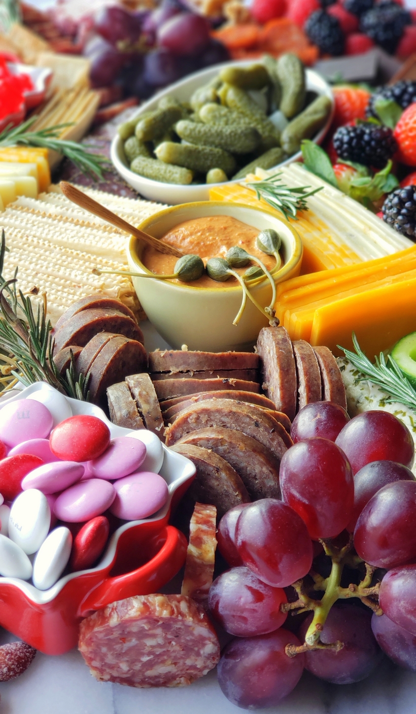 Valentine's Day Charcuterie Board close-up. A close-up of the savory elements, including beef summer sausage, pepper Genoa salami, caper berries, and cornichons, arranged neatly on the Valentine's Day charcuterie board.