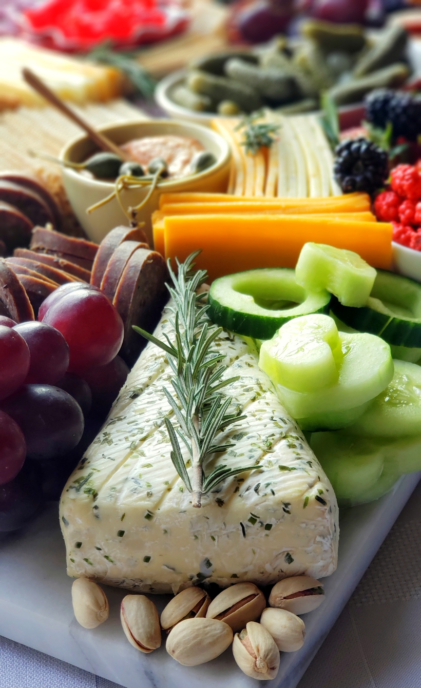 Valentine's Day Charcuterie Board with pistachios. An overhead shot of the charcuterie board, featuring layers of sliced meats, cheeses, crackers, fresh fruit, nuts, and chocolates, with rosemary sprigs adding a decorative touch.