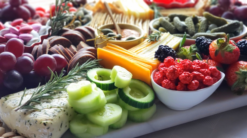Valentine's Day Charcuterie Board with cucumbers. A close-up of the savory elements, including beef summer sausage, pepper Genoa salami, caper berries, and cornichons, arranged neatly on the board.