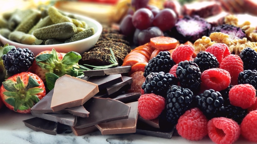 Valentine's Day Charcuterie Board with chocolate and berries. A sweet section of the charcuterie board showcasing Valentine-themed M&M’s, chocolate hearts, raspberry pretzels, cinnamon bears, and French burnt peanuts.