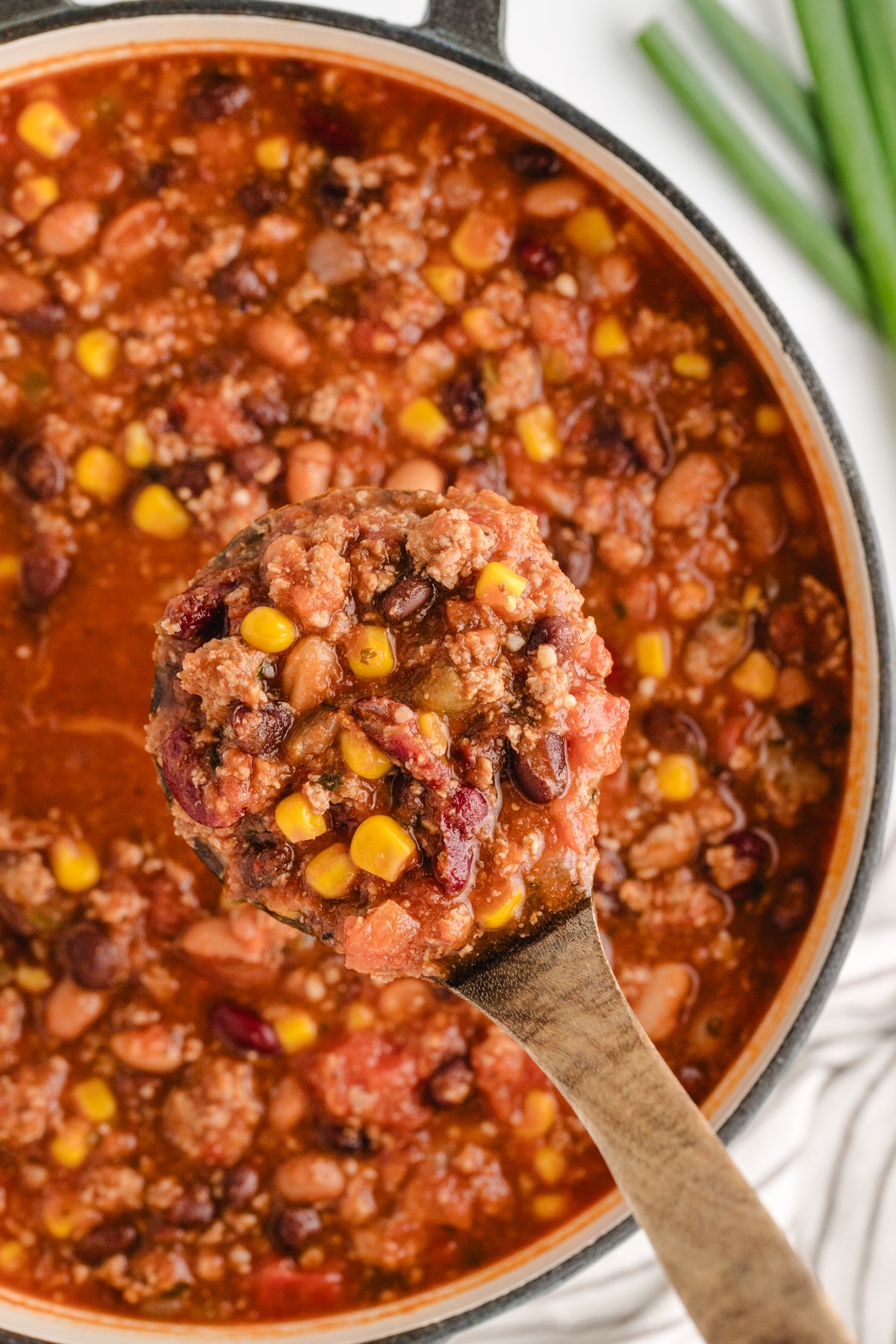 Low Calorie Chili in Dutch Oven Ladle lifting a serving of low calorie chili with turkey, beans, and corn from a Dutch oven.