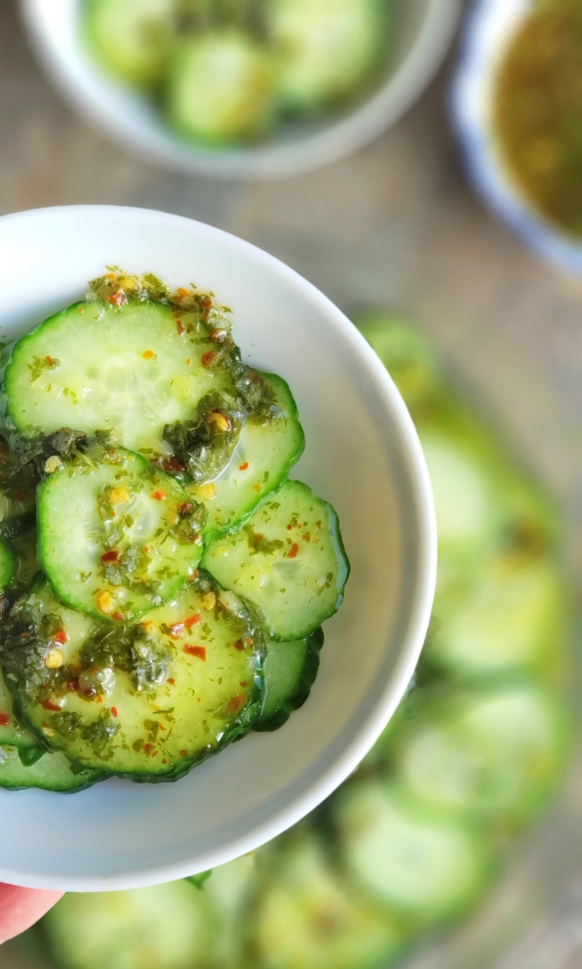 Keep it light and refreshing ~ Cucumbers with Mint Vinaigrette are the perfect side dish for any meal. They are especially wonderful with Asian Cuisine. #cucumbers #sidedish #asiancuisine Sliced cucumbers in a bowl topped with vinaigrette.
