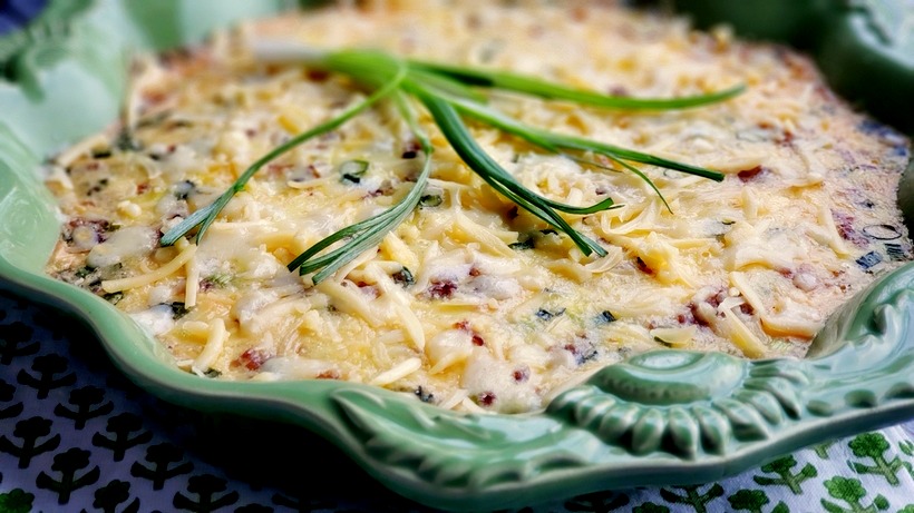A decadent and sumptuous brunch recipe, this Mouthwatering Oven Omelet will have you wondering why you make eggs any other way. Everyone at your breakfast table will imagine you fussed over this easy omelet, when in reality this egg dish takes very little time to put together. #noblepig #ovenomeletterecipe #ovenomelet #breakfastcasserole #brunchrecipe #bakedomelette #bakedomelet #bruncheggs #bruncheggsforacrowd #bruncheggideas #breakfastfordinner #bruncheggscasserole #brunchideas Omelet in a green dish on a printed napkin.