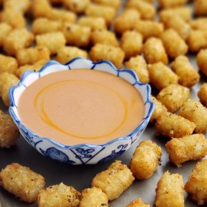 Tater tots surrounding a bowl of sauce on a tray.