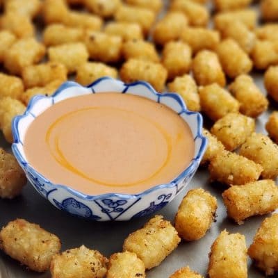 Tater tots surrounding a bowl of sauce on a tray.