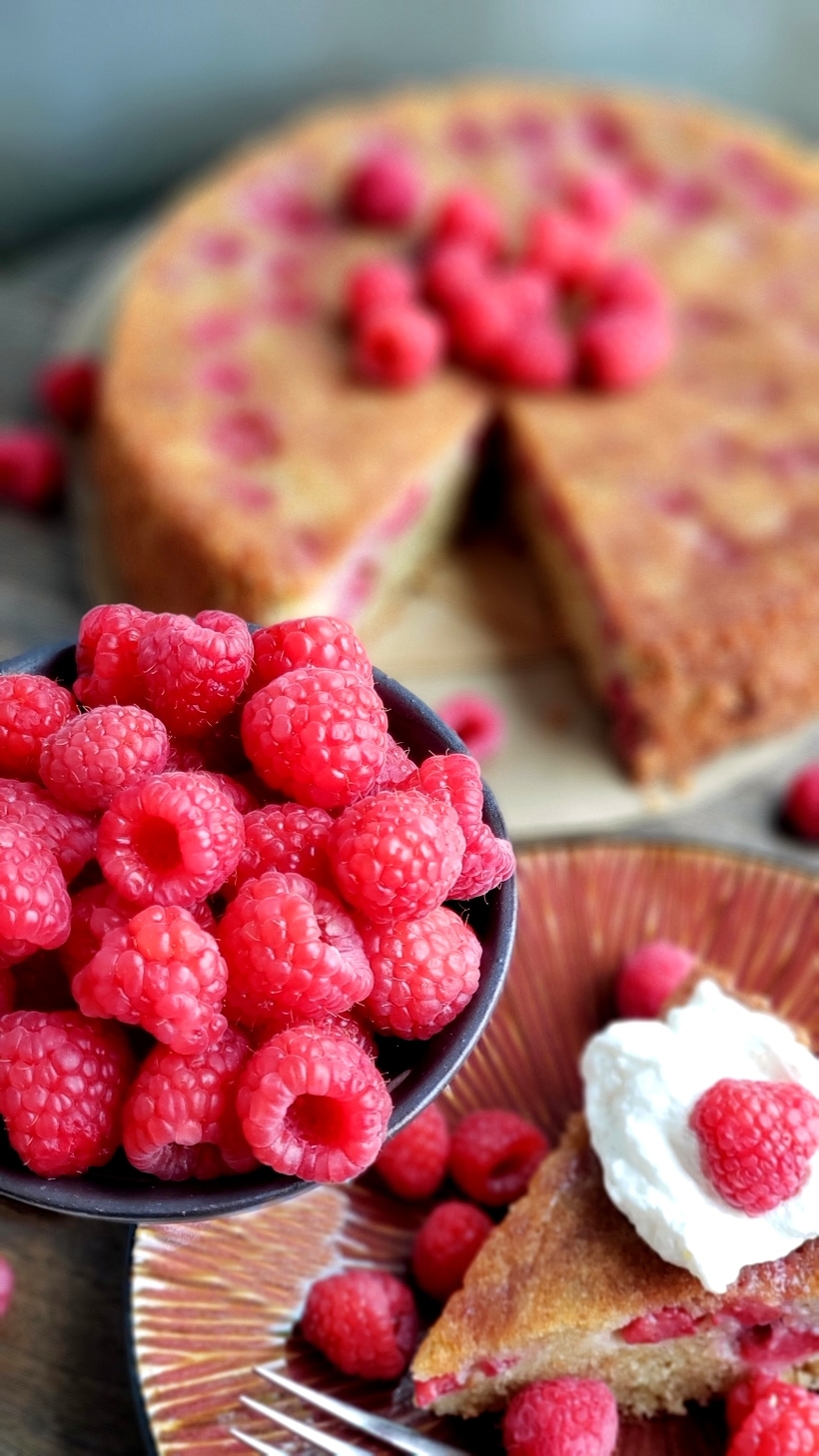 Raspberry cake whole with a slice with whipped cream on top.