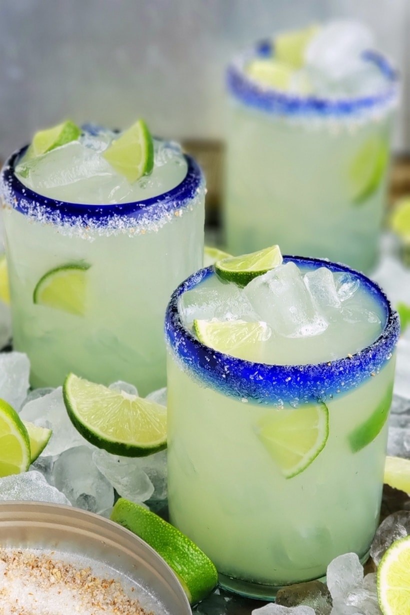 Three agave margaitas in glasses surrounded by ice and lime.