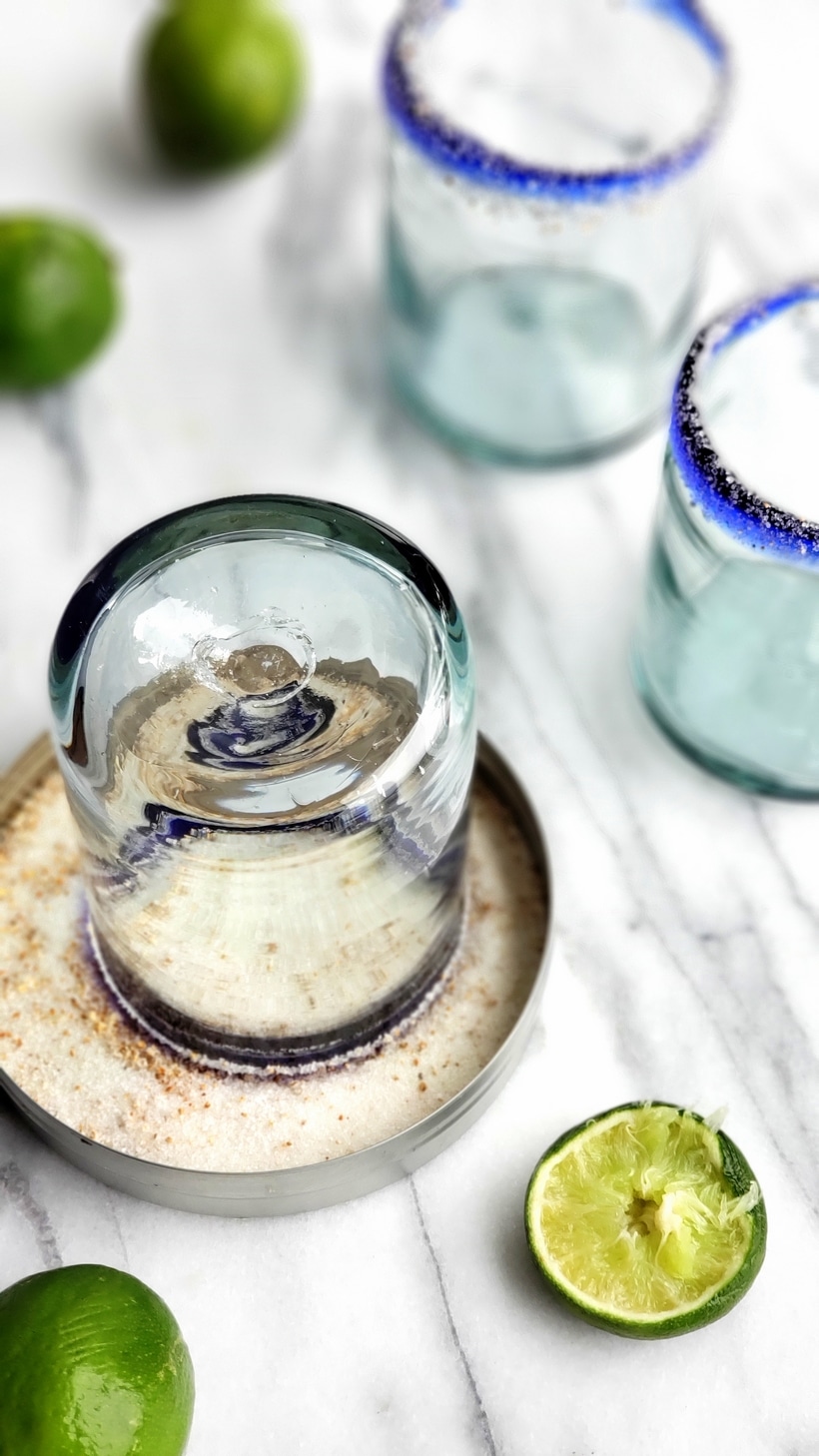 Empty margaritas with salted rims and a glass sitting in margarita salt.