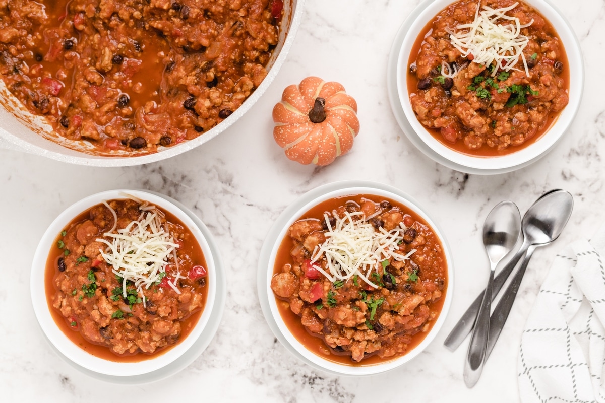 Pumpkin chili with ground turkey served in white bowls topped with shredded cheese and herbs.
