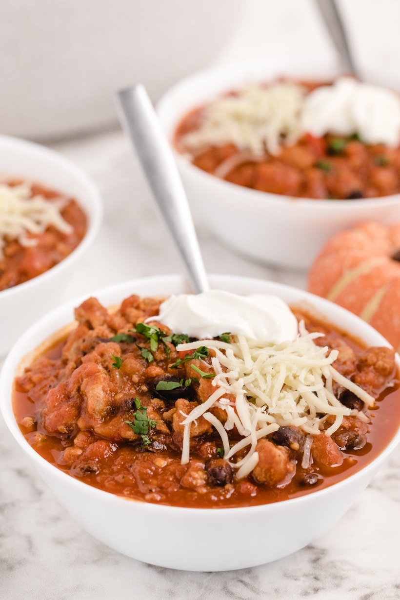 Bowl of hearty pumpkin chili topped with sour cream, shredded cheese, and cilantro.