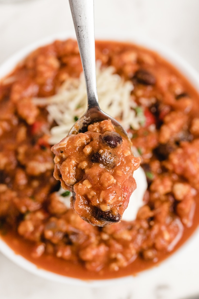 Close-up of a spoon lifting pumpkin chili with black beans and turkey.