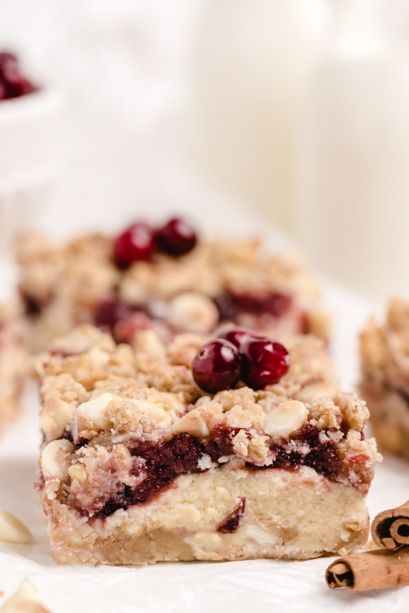 Cranberry Bars with Cheesecake Filling and Oat Crumble Close-up of cranberry bars with creamy cheesecake filling and oat crumble on parchment.