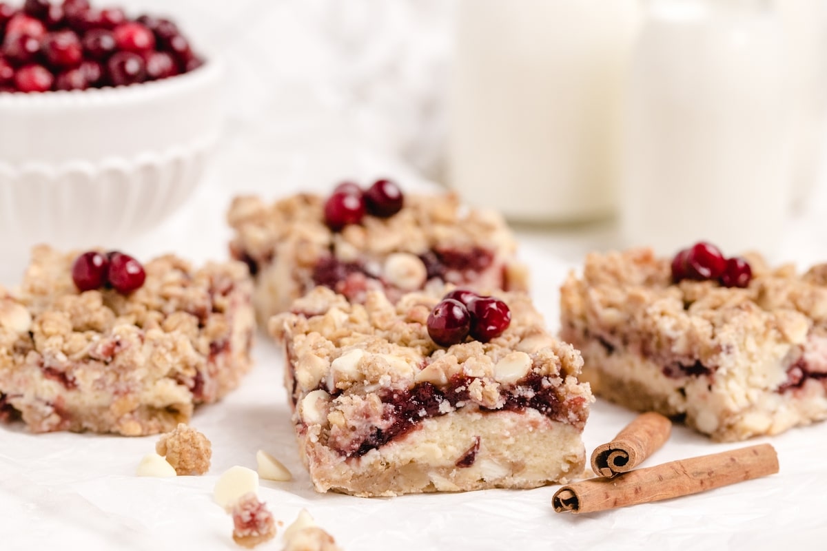 Sliced Cream Cheese Cranberry Bars with Oat Topping Cranberry cream cheese bars sliced into squares with a golden oat topping on parchment paper.