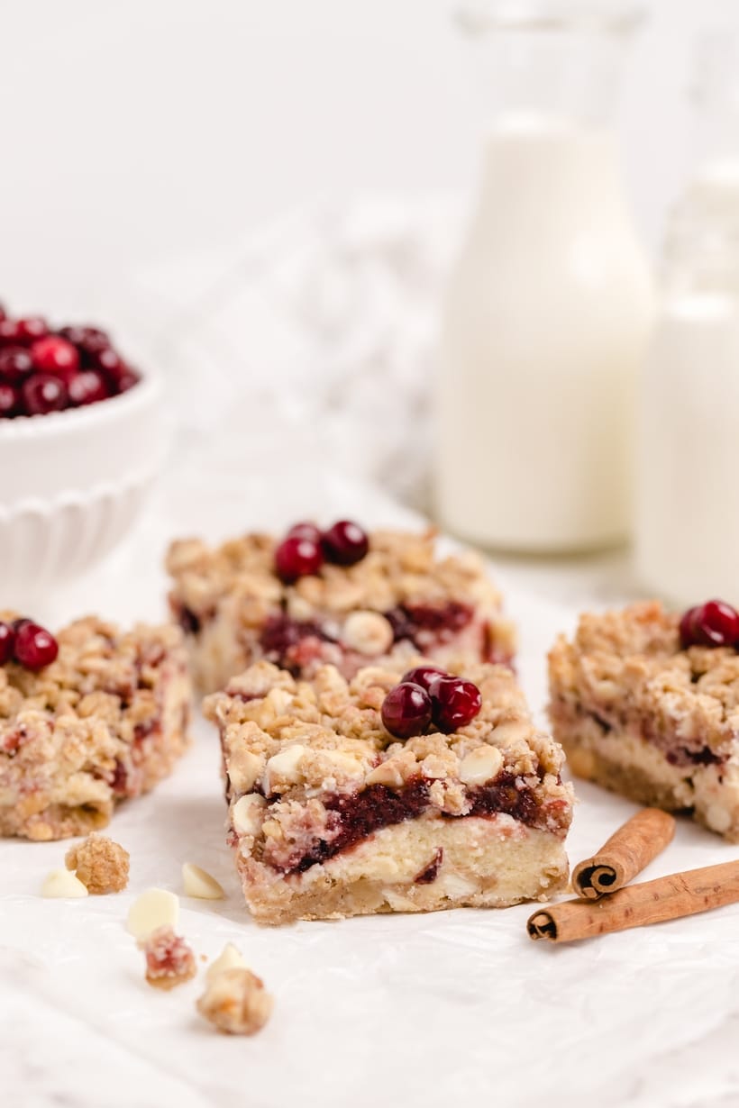 Stacked Cranberry Bars with Cheesecake Layers Festive cream cheese cranberry bars stacked to show layers of creamy filling, cranberry sauce, and oat crust.