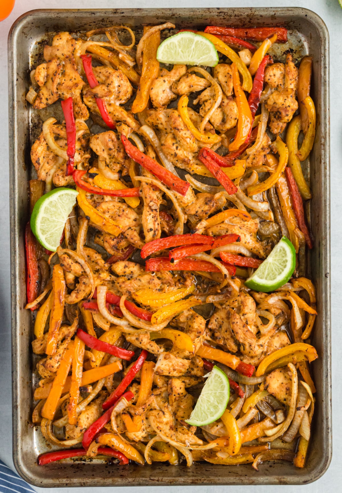 Bake Sheet Pan Chicken Fajitas A sheet pan filled with baked chicken fajitas, garnished with lime wedges, ready to serve.